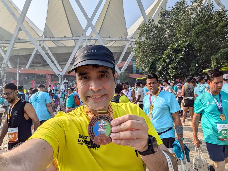 Vikram smiling and holding up his finisher's medal outside Jawaharlal Nehru Stadium after the race